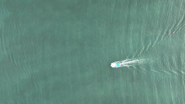 قارب يتحرك في مياه ميناء جازان، تصوير درون من الأعلى.