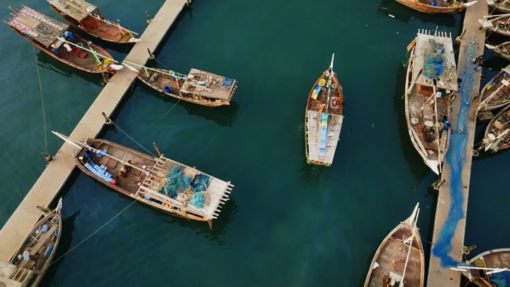 قوارب خشبية راسية في ميناء جازان مع وجود قارب يستعد للتوقف، تصوير درون من الأعلى.