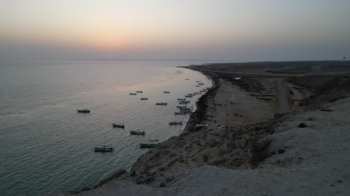 شاطئ جزيرة فرسان في جازان مع قوارب صغيرة عند الغروب، تصوير درون.
