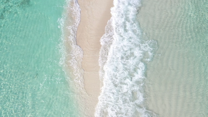 Waves crashing on a sandy beach with blue waters in the Asir region, aerial shot.