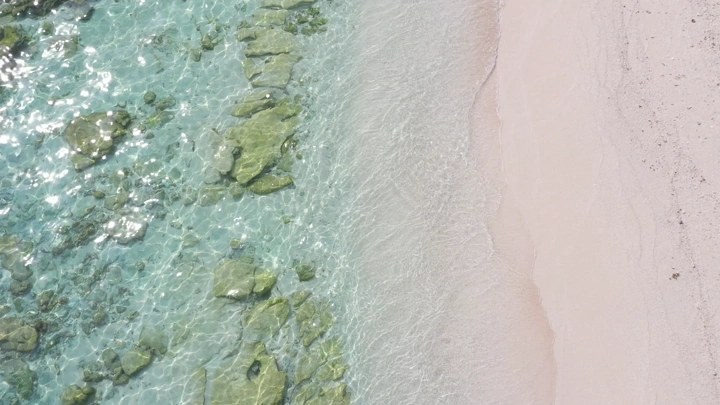 A sandy beach and clear waters with wave movement in the Asir region, aerial shot.