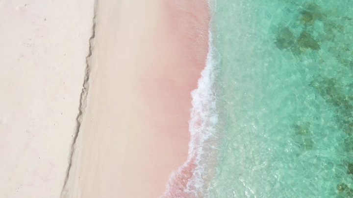 A pink sandy beach and clear blue waters in the Asir region, aerial shot.