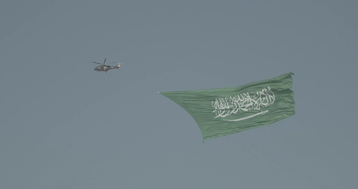 Helicopter carrying Saudi flag in the sky, aerial shot.