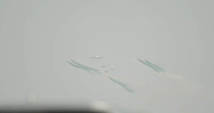 Air show with planes releasing colored smoke in the sky, distant shot.