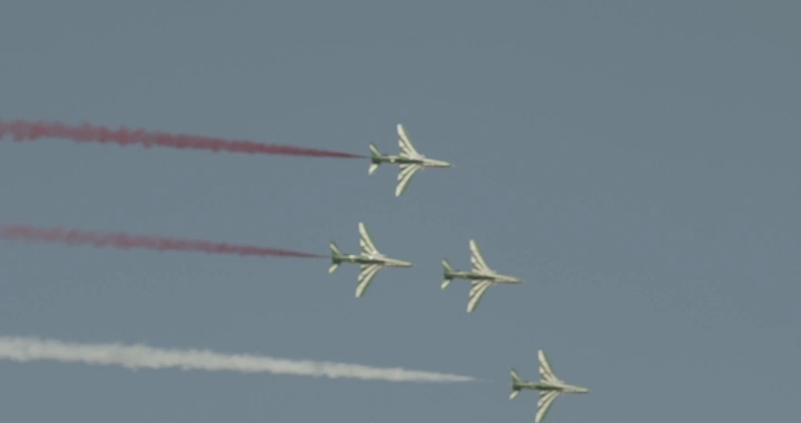 Planes in aerial formation with colored smoke in the sky, shot from below.