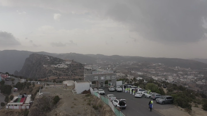 An aerial shot of Al-Sahab Park in Abha with cars and people, on a cloudy day.