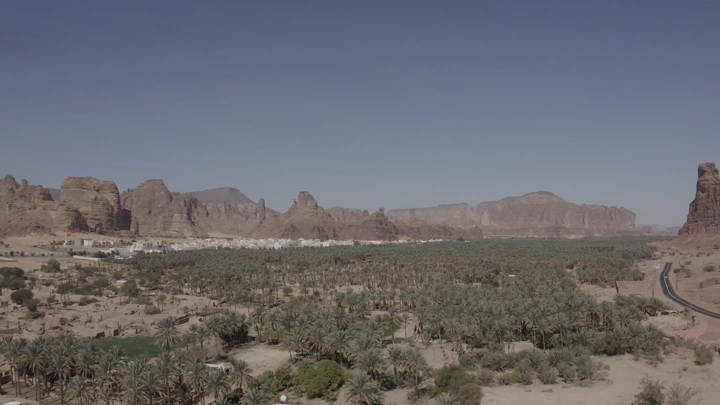 Aerial view of AlUla Old Town with mountains and palm trees, daytime shot.