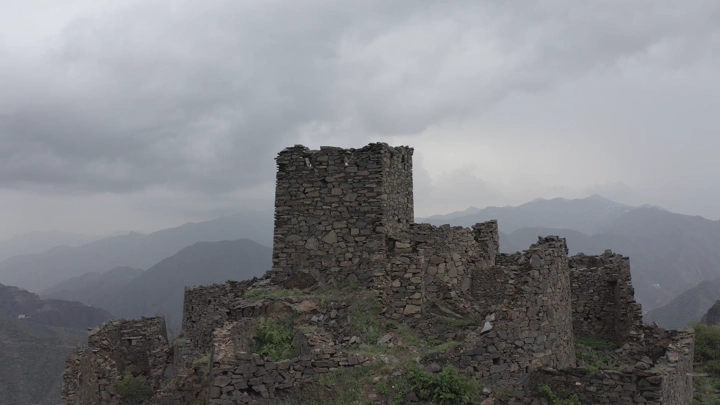 An ancient stone castle in Rijal Almaa under a cloudy sky in the Asir region, aerial shot.