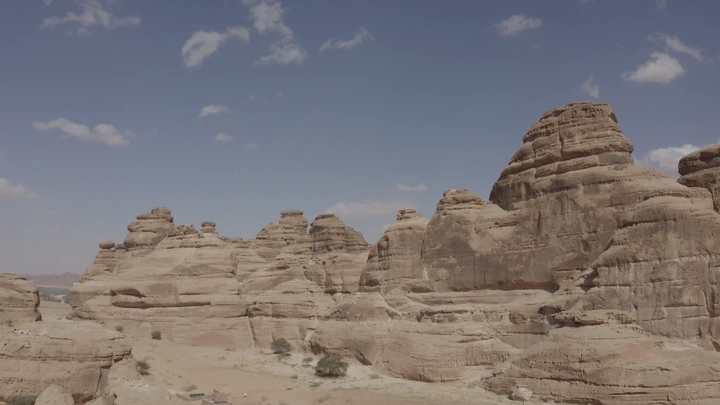 Rock formations in AlUla mountains under blue sky, aerial shot.