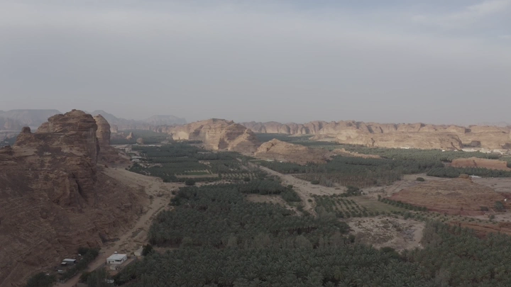 Mountains and farms in AlUla under a cloudy sky, aerial shot.