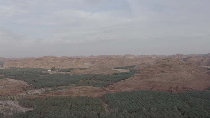 Mountains and farms in AlUla under cloudy sky, aerial shot.