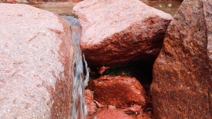 ينابيع تتدفق بين صخور حمراء في جبال أجا، تصوير قريب.