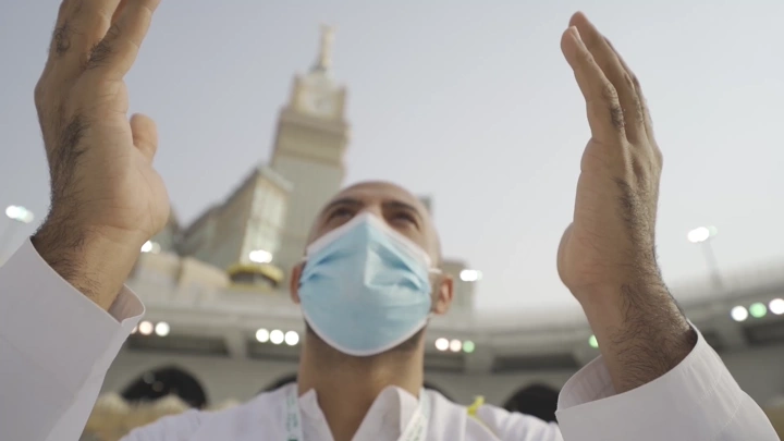 شخص يرتدي كمامة يرفع يديه في الحرم المكي، لقطة من الأسفل.