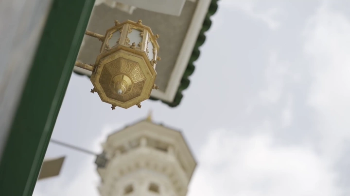 فانوس ذهبي في الحرم مع مئذنة في الخلفية، لقطة بزاوية منخفضة.