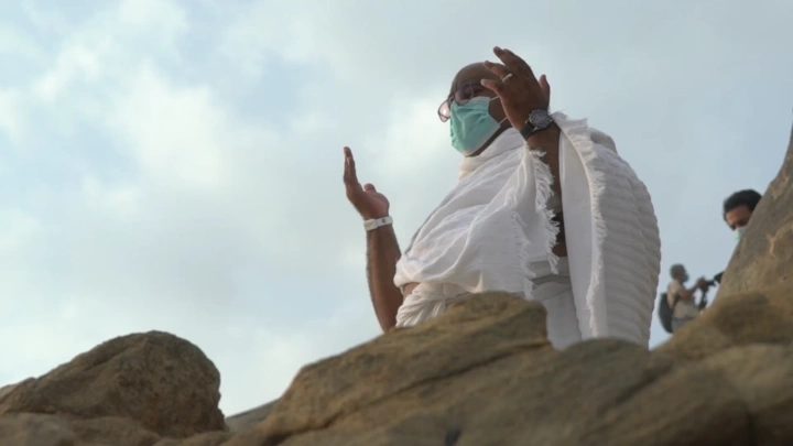 شخص يرتدي إحرامًا يقف على جبل أثناء الحج، لقطة من الأسفل.