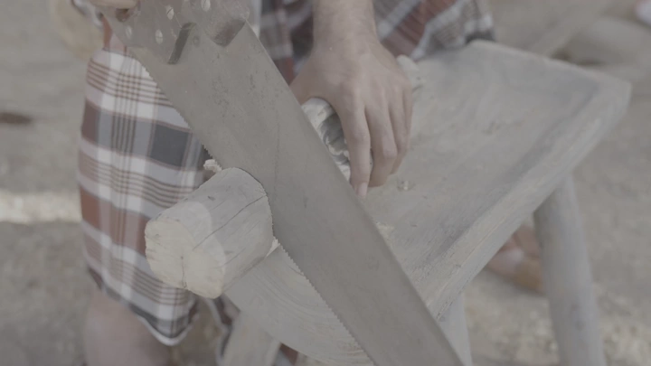 نجار يعمل على قطعة خشب بمنشار يدوي، لقطة قريبة.