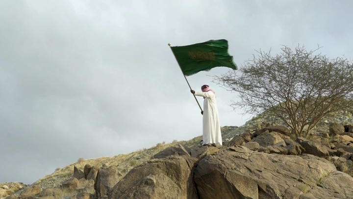 رجل يرفع علمًا أخضر على تلة صخرية، لقطة واسعة.
