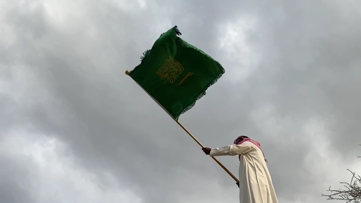 رجل يرفع علمًا أخضر في يوم غائم، لقطة من الأسفل.