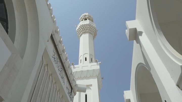 مئذنة مسجد بيضاء تحت سماء زرقاء، لقطة من الأسفل.