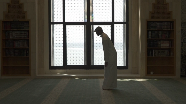 Man praying in sunlit mosque, side shot.