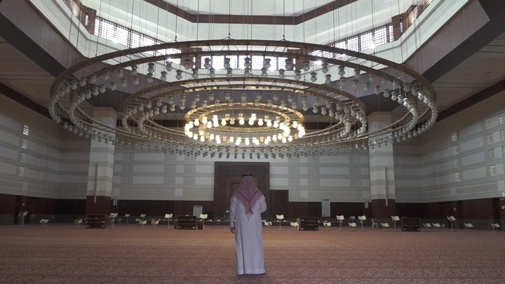 رجل يقف في مسجد كبير تحت ثريا ضخمة، لقطة داخلية.