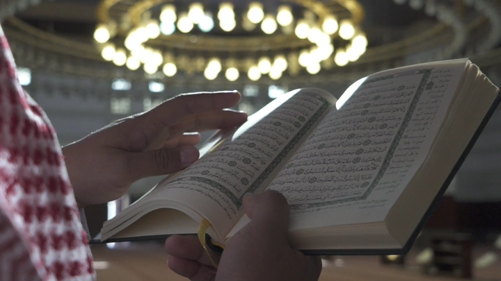 شخص يقرأ القرآن في مسجد تحت إضاءة الثريا، لقطة قريبة.