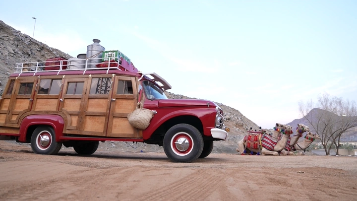 سيارة قديمة وجمال في الصحراء، لقطة جانبية.