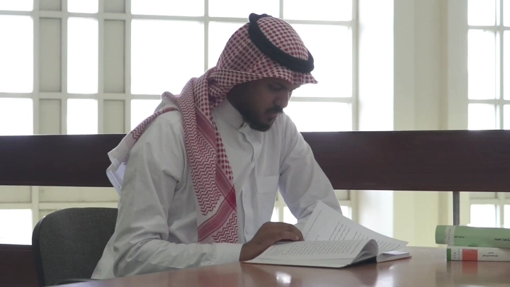 طالب يقرأ في مكتبة جامعية، لقطة داخلية.