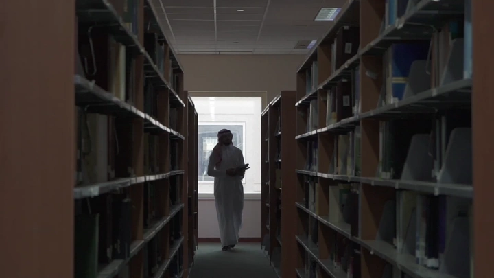 شخص يسير في ممر مكتبة جامعية، لقطة داخلية.