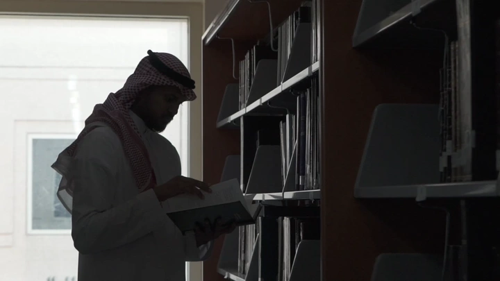 رجل يقرأ كتابًا في مكتبة جامعة، لقطة جانبية.