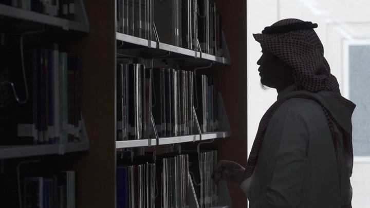 شخص يرتدي الزي التقليدي في مكتبة جامعة، لقطة ظلية.