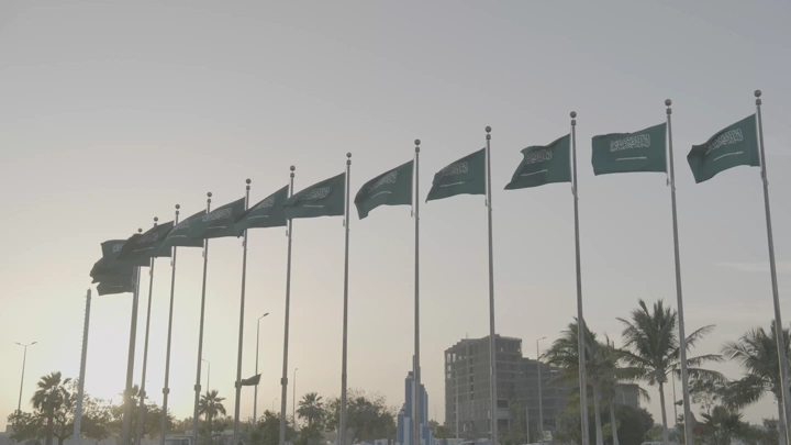 أعلام سعودية ترفرف في جدة عند الغروب، لقطة واسعة.