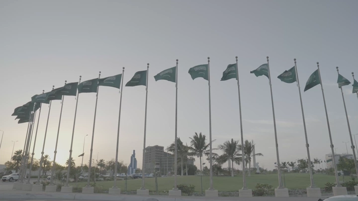 أعلام سعودية ترفرف في جدة عند الغروب، لقطة واسعة.
