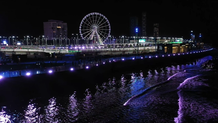 عجلة فيريس مضاءة ليلاً على كورنيش جدة، لقطة ليلية.