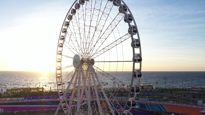 Ferris wheel on Jeddah Corniche at sunset, aerial shot.