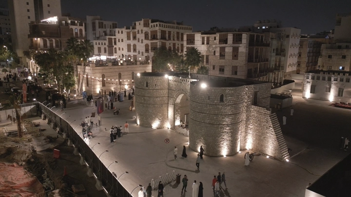 بوابة تاريخية مضاءة في جدة القديمة ليلاً، لقطة جوية.