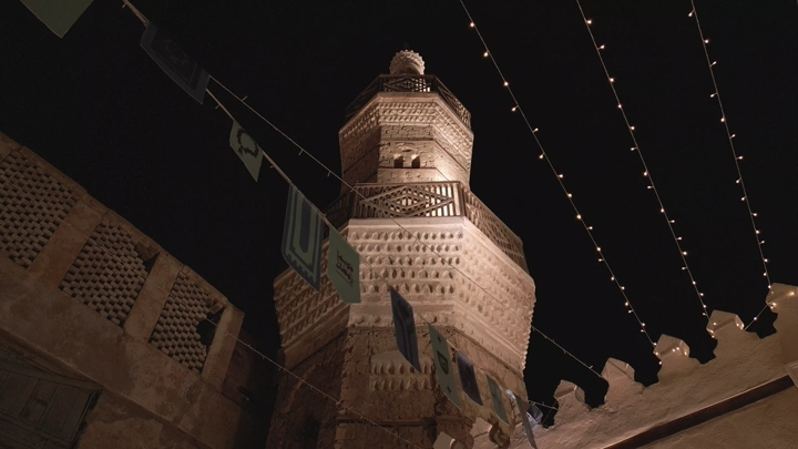 مئذنة في جدة القديمة مضاءة ليلاً، زاوية منخفضة.