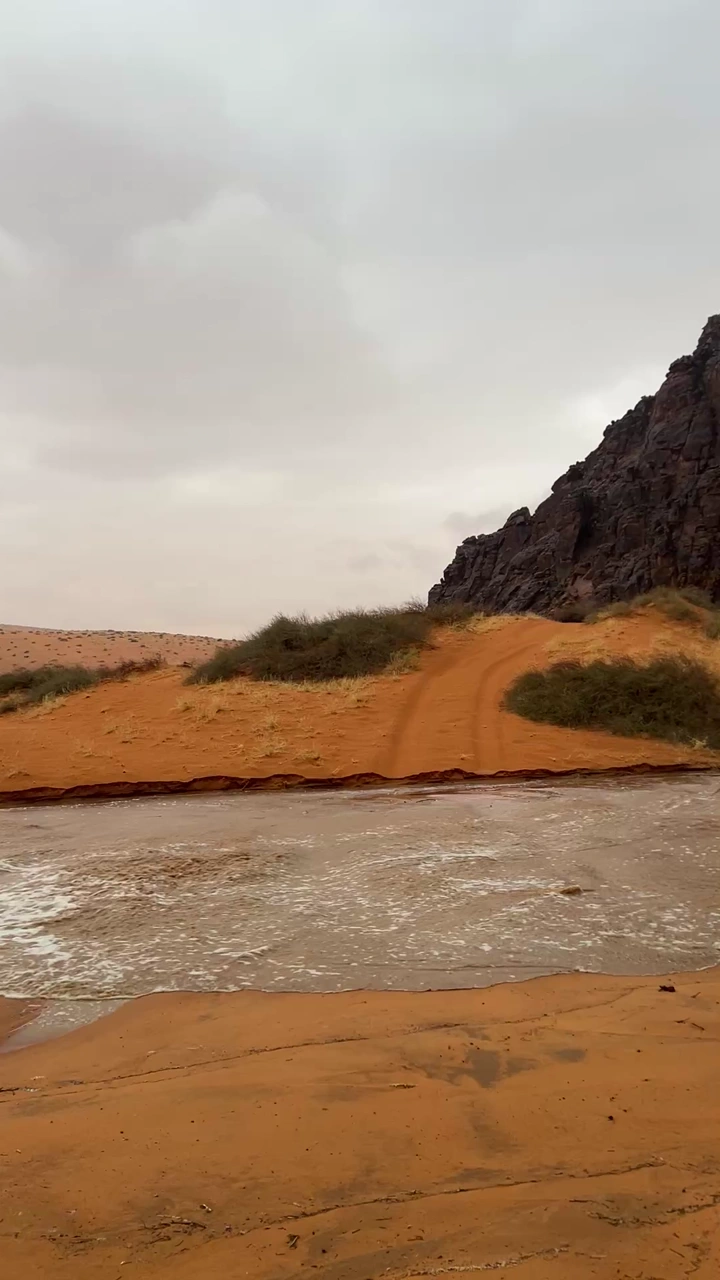 سيل في صحراء النفود مع جبل في الخلفية، لقطة نهارية.