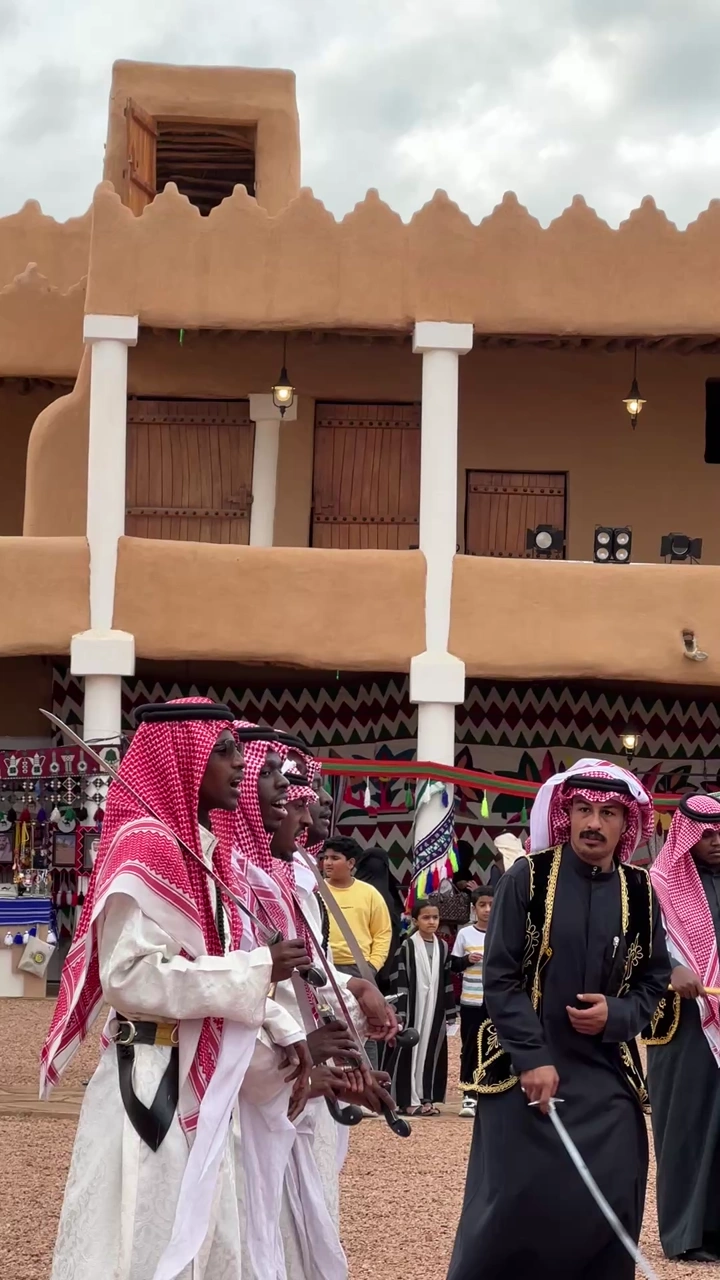 عرضة سعودية أمام مبنى طيني تقليدي، لقطة نهارية.