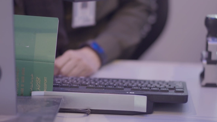 موظف يفحص جواز سفر سعودي في كاونتر المطار، لقطة مقربة.