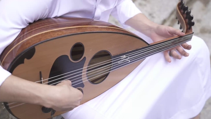 لقطة مقرّبة لشخص يعزف العود في مكان خارجي، لقطة نهاري.