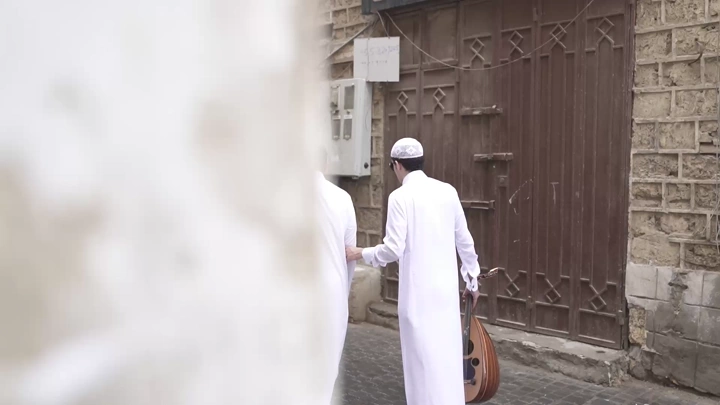 شاب عربي يساعد رجل كفيف في شارع قديم، لقطة من الخلف.