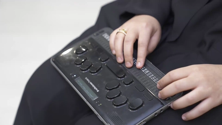 سيدة تستخدم جهاز برايل الإلكتروني للقراءة، لقطة مقربة.