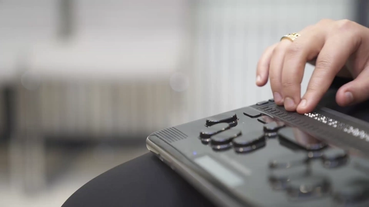 لقطة مقربة لسيدة تقرأ بجهاز برايل إلكتروني، لقطة داخلي.