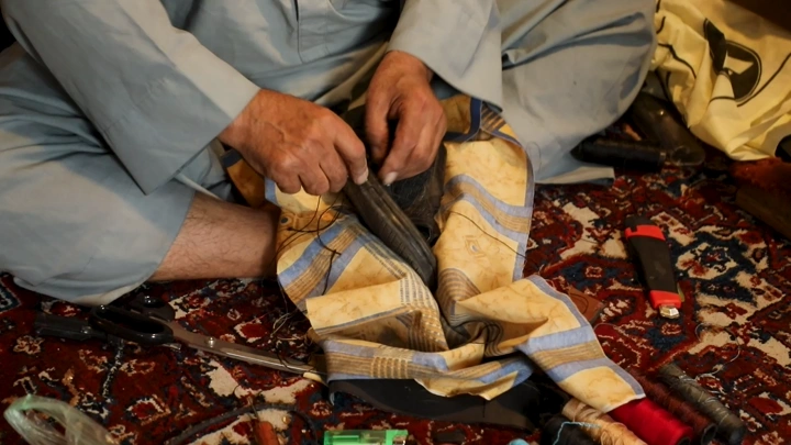 حرفي يصلح حذاء تقليدي يدوياً على سجادة مزخرفة، لقطة مقرّبة.