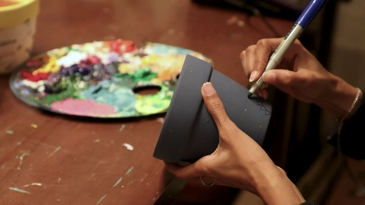 فنان يرسم على إناء زهور خزفي، لقطة مقرّبة.