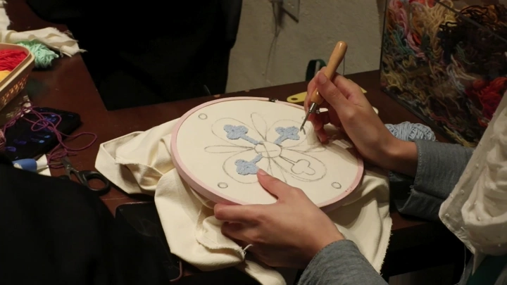 صورة مقرّبة لشخص يقوم بالتطريز اليدوي في غرفة، لقطة علوية.