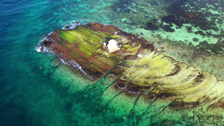 جزيرة كدمبل في جازان، لقطة جوية تُظهر التكوينات الصخرية والمياه الزرقاء.
