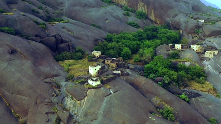 قرية غيه في منطقة عسير محاطة بالصخور والأشجار، لقطة جوية.