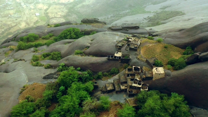 Ghey village in Asir region, aerial view showing houses among rocks and trees.